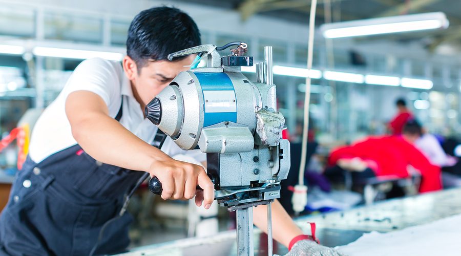 Indonesian worker using a cutter - a large machine for cutting fabrics - in a asian textile factory, he wears a chain glove